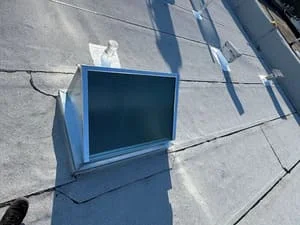 Blue-framed skylight installed on flat roof with aluminum flashing and sealed joints