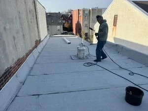 Worker installing flat roof membrane on commercial building with rooftop equipment and materials visible