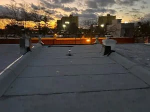 Flat roof membrane installation on commercial building with rooftop equipment and city skyline
